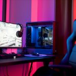 A sleek gaming setup featuring a high-end PC, widescreen monitor, and ergonomic chair lit by neon lights.